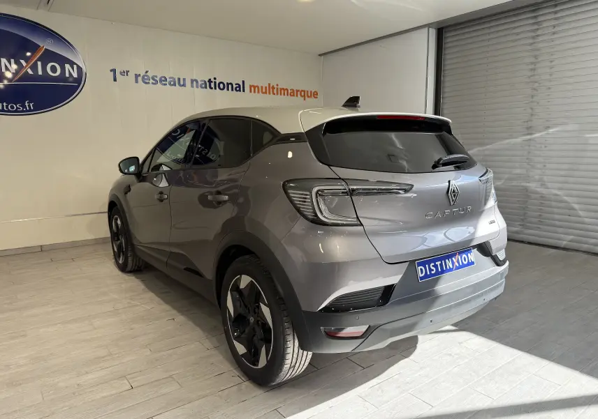 Vue 3/4 arrière gauche du Renault Captur gris Cassiopée métal avec toit gris et jantes noires en intérieur showroom.