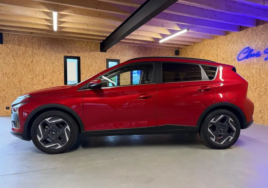 Profil côté gauche du Hyundai Bayon rouge 2025 avec jantes alu 17'' et rétroviseurs électriques dans un garage.