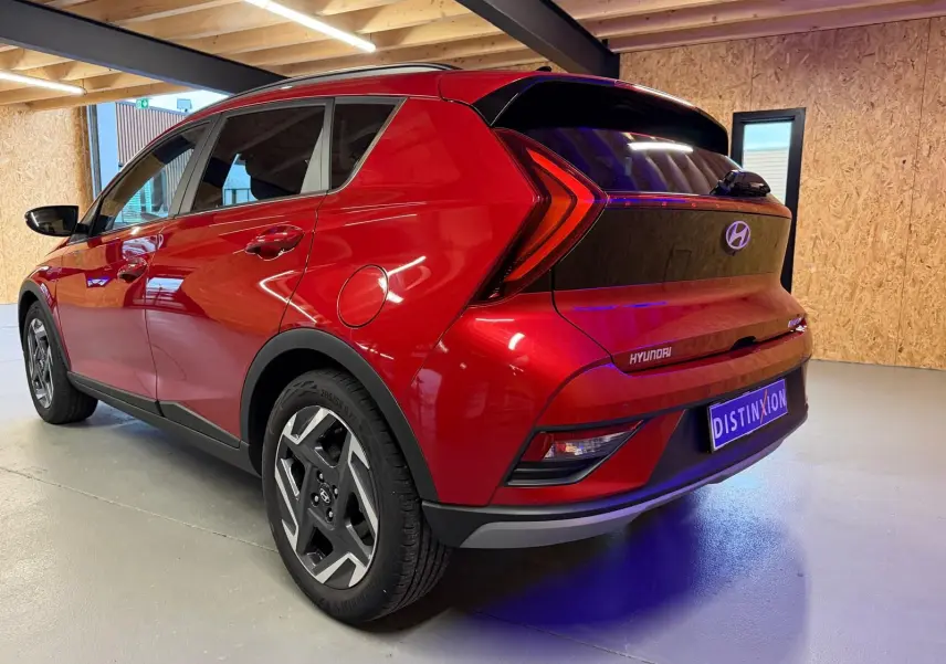 Vue 3/4 arrière droite d'une Hyundai Bayon rouge avec calandre noir laqué et jantes alu 17 pouces dans un garage.