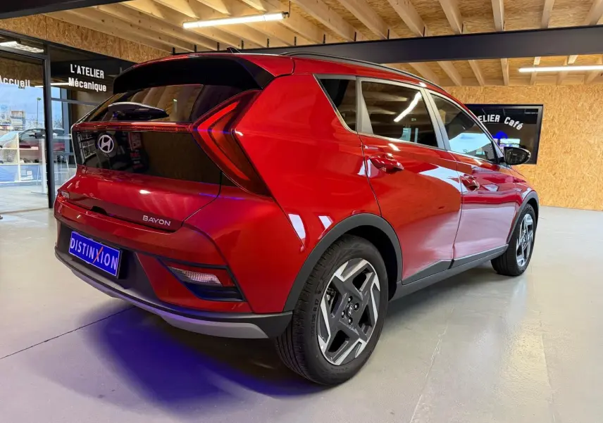 Vue 3/4 arrière droite du Hyundai Bayon rouge avec calandre noir laqué et jantes alu 17 pouces dans un showroom.