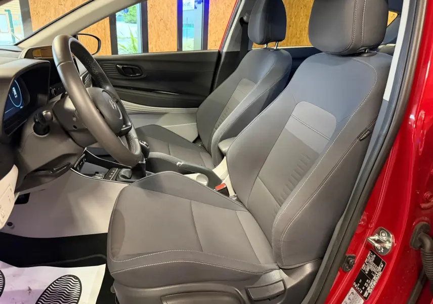Vue intérieure côté conducteur du Hyundai Bayon rouge 2025, sièges tissu gris et volant cuir multifonctions.