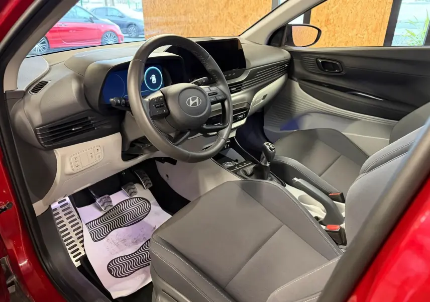 Vue intérieure côté conducteur de la Hyundai Bayon rouge 2025, avec tableau de bord moderne et volant cuir multifonctions.