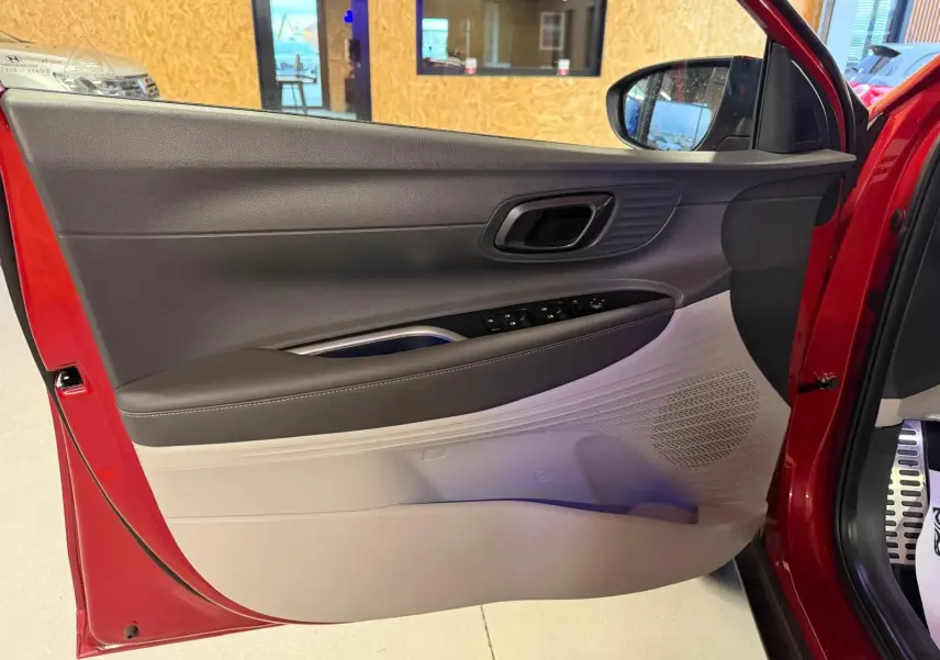 Porte avant gauche ouverte d'une Hyundai Bayon rouge 2025, intérieur bi-ton noir et gris clair avec commandes électriques.