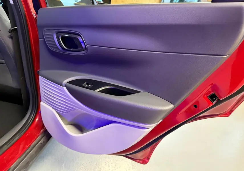 Vue rapprochée de la porte arrière gauche rouge d'une Hyundai Bayon avec panneau intérieur noir et gris clair.