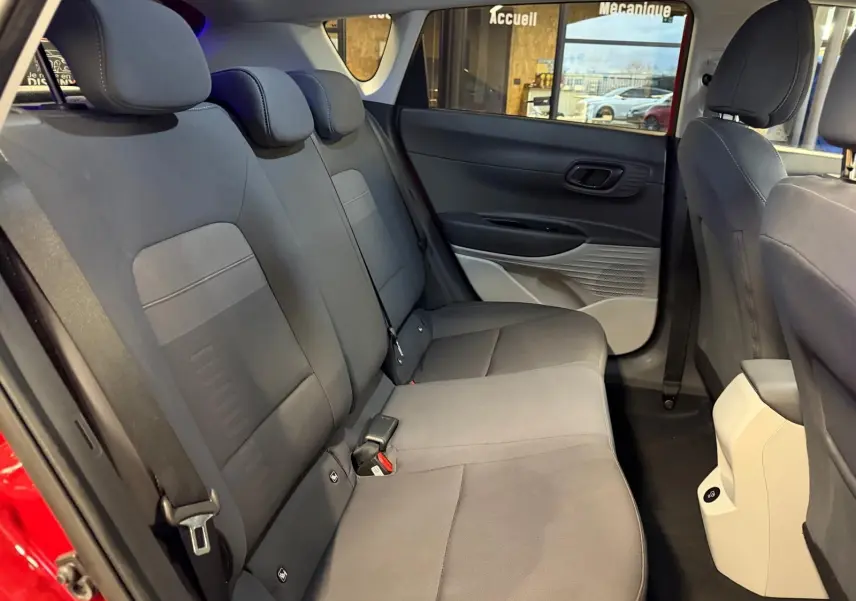 Vue intérieure arrière côté gauche du Hyundai Bayon rouge 2025, montrant la banquette grise et les portes ouvertes.