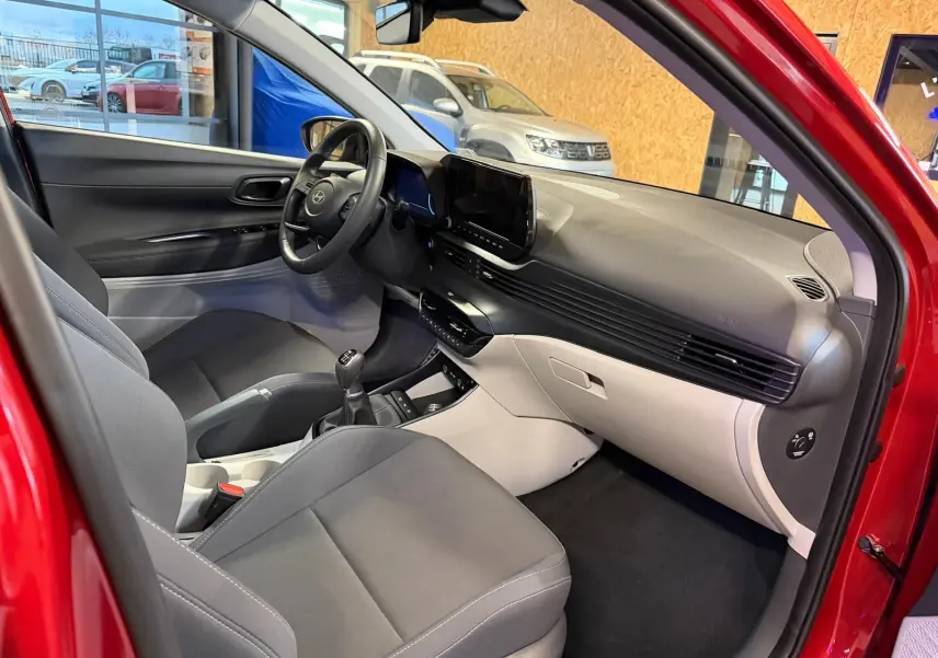 Intérieur bi-ton noir et gris clair du Hyundai Bayon rouge, vue côté passager avant avec tableau de bord moderne et écran tactile.