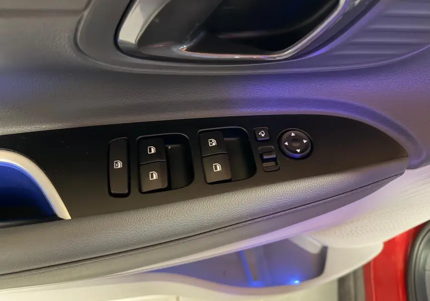 Gros plan sur les commandes de vitres et rétroviseurs côté gauche d'une Hyundai Bayon rouge avec éclairage d'ambiance bleu.