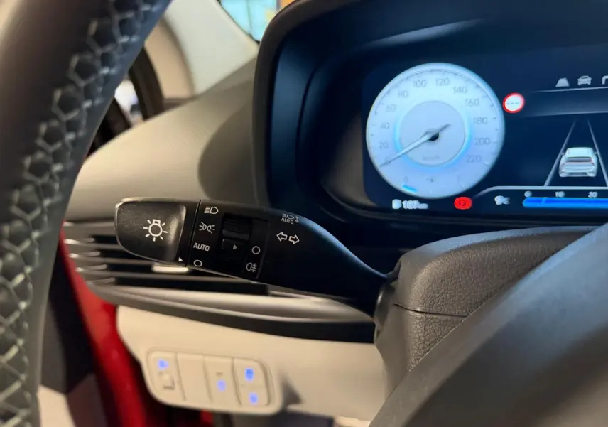 Gros plan sur la manette des feux et le tableau de bord numérique bleu d'une Hyundai Bayon rouge, côté gauche.