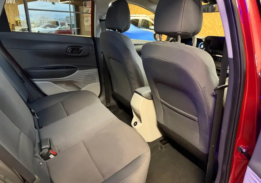 Vue arrière côté gauche de l'intérieur du Hyundai Bayon rouge 2025, sièges tissu gris et console centrale beige.