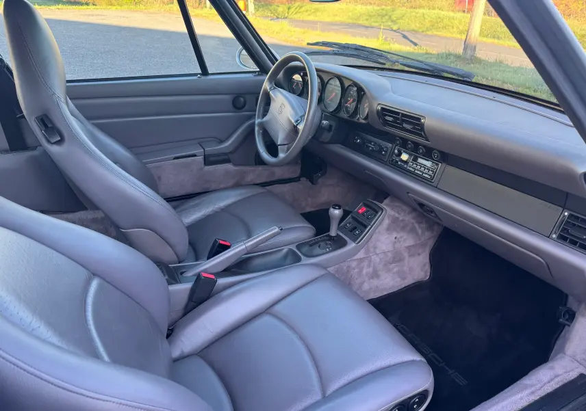 Vue intérieure côté conducteur de la Porsche 911 Carrera 993 de 1996 avec sellerie cuir gris et tableau de bord épuré.
