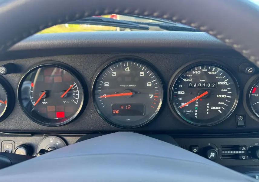 Vue rapprochée du tableau de bord et des compteurs noirs d'une Porsche 911 Carrera 2 gris polaire de 1996.