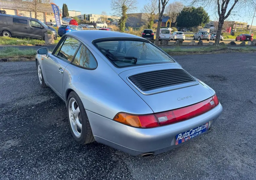 Vue 3/4 arrière droite d'une Porsche 911 Carrera 993 gris polaire avec jantes 17 pouces sur parking extérieur.