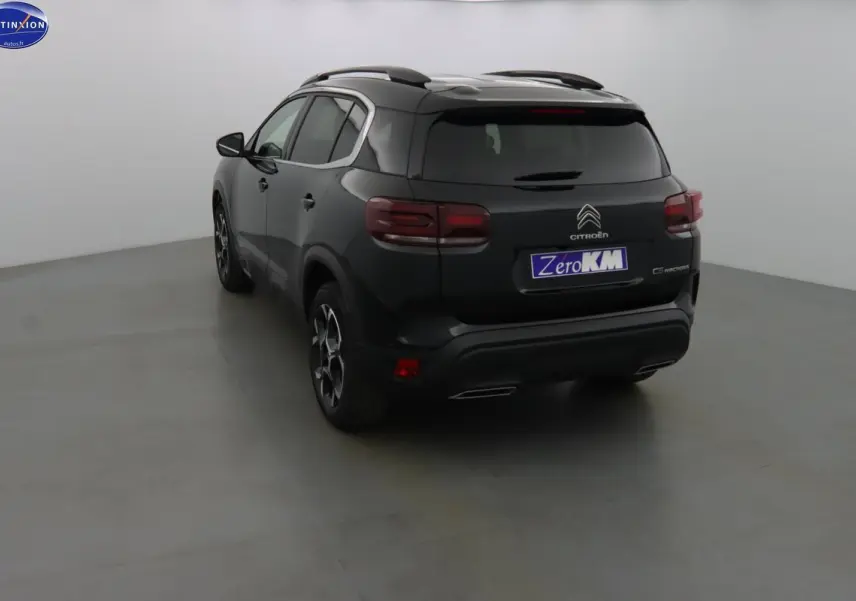 Vue 3/4 arrière d'un Citroën C5 Aircross noir métal avec jantes bi-ton et barres de toit visibles.