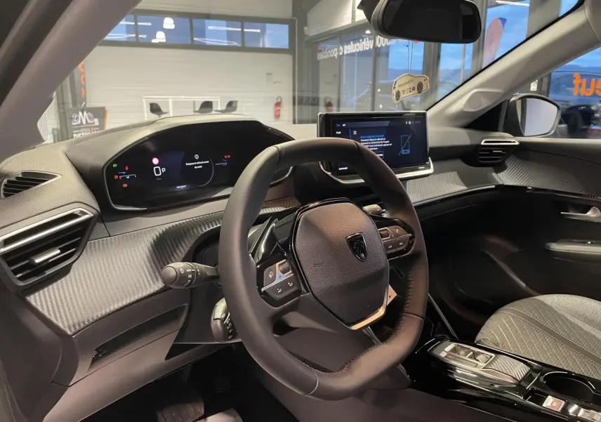 Vue intérieure côté conducteur du Peugeot 208 1.2i Hybrid 2025, volant compact et tableau de bord numérique.
