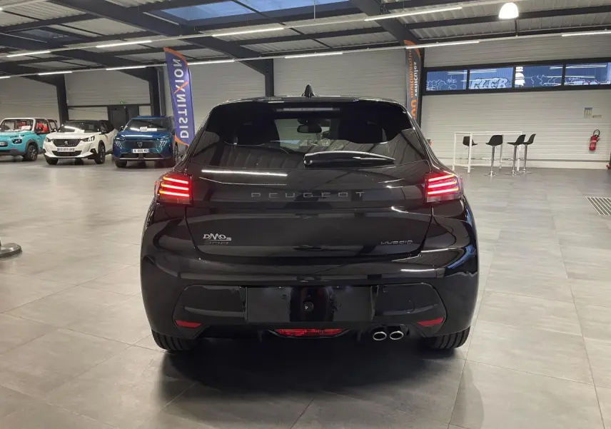 Vue arrière d'une Peugeot 208 hybride noire métallisée avec feux arrière allumés en intérieur showroom.