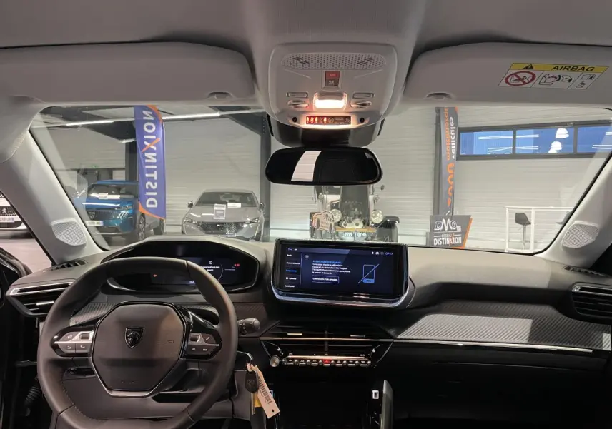 Vue intérieure avant du tableau de bord de la Peugeot 208 noire métallisée avec écran tactile central et volant compact cuir.