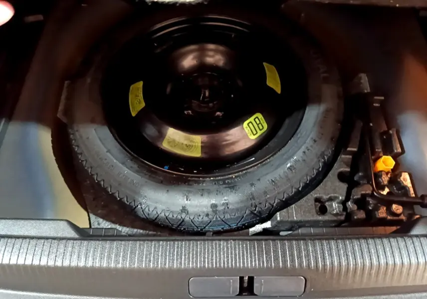 Vue plongeante sur la roue de secours noire et les outils de bord dans le coffre d’un Peugeot 2008 bleu.