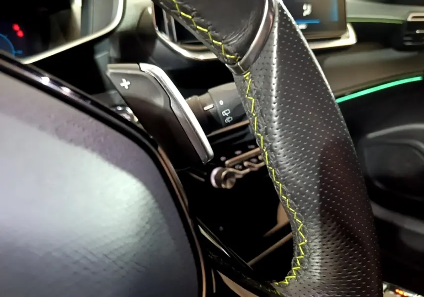 Gros plan sur le volant cuir noir avec surpiqûres jaunes et palettes de changement de vitesse dans l’habitacle du Peugeot 2008 bleu.