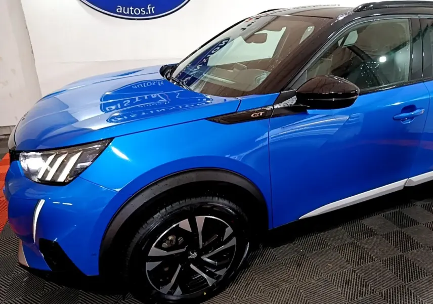 Vue 3/4 avant gauche d’un Peugeot 2008 GT bleu avec jantes noires et toit noir brillant.