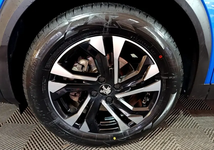 Gros plan sur la roue avant droite du Peugeot 2008 bleu, mettant en valeur la jante alliage bicolore au design moderne.