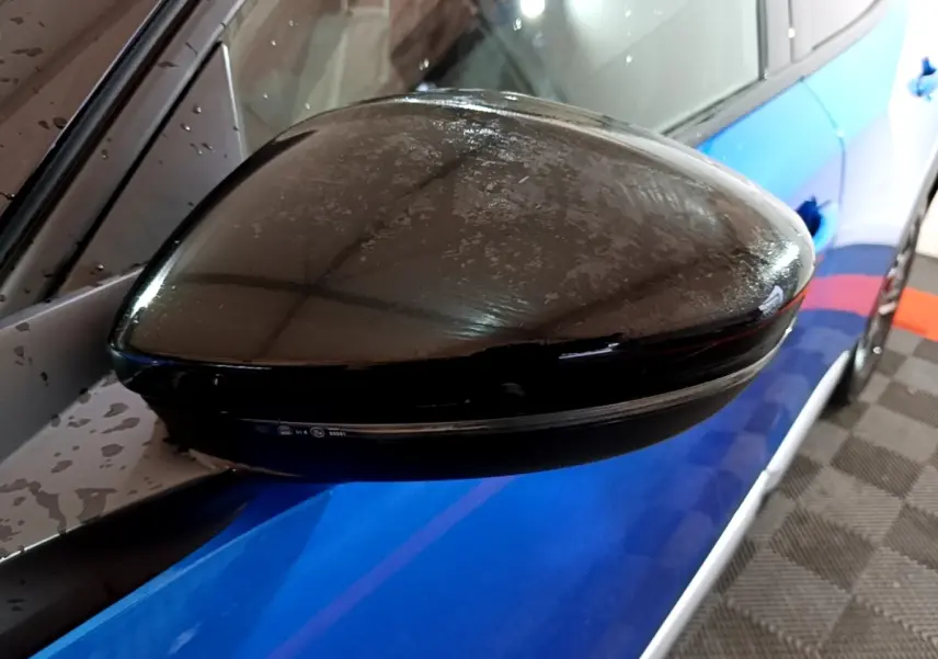 Gros plan sur le rétroviseur noir côté gauche d’un Peugeot 2008 bleu visible en arrière-plan.