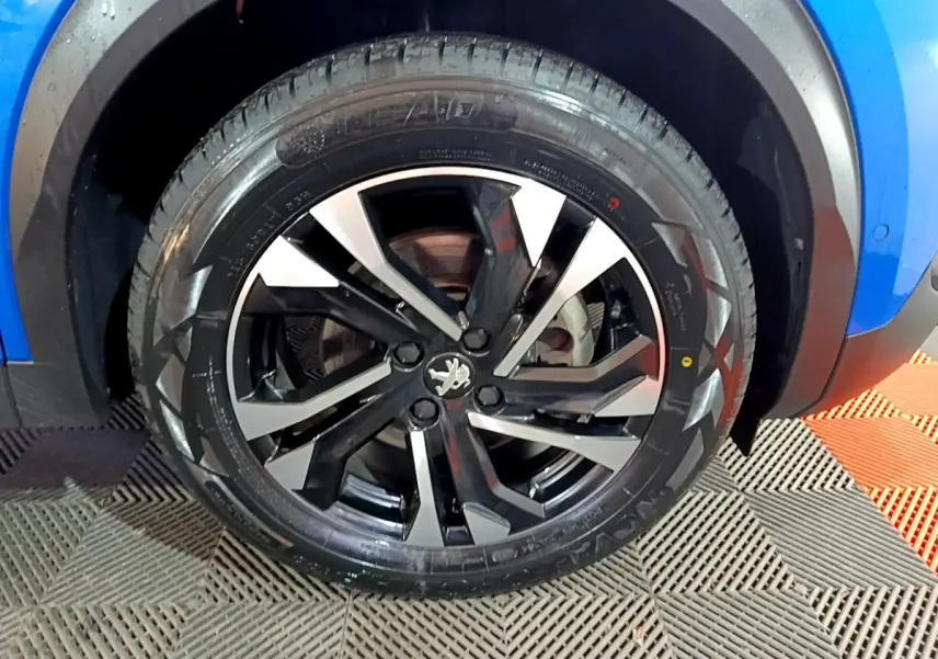 Gros plan sur la roue avant droite d’un Peugeot 2008 bleu, avec jante alliage noire et argentée au design moderne.