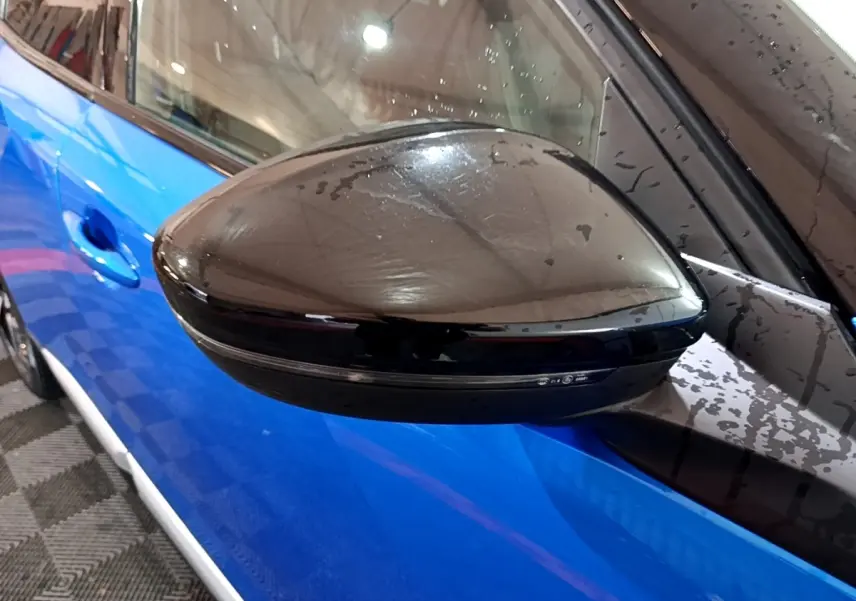Rétroviseur noir en gros plan côté gauche sur la carrosserie bleue d’un Peugeot 2008 GT 2021.