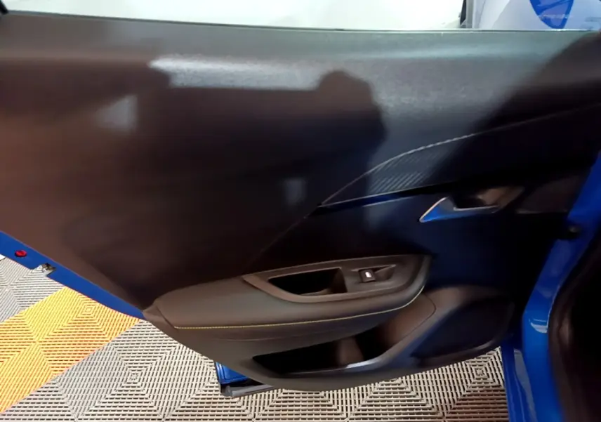Vue rapprochée de la porte arrière gauche bleu vif du Peugeot 2008 GT avec poignée intérieure et bouton de lève-vitre.