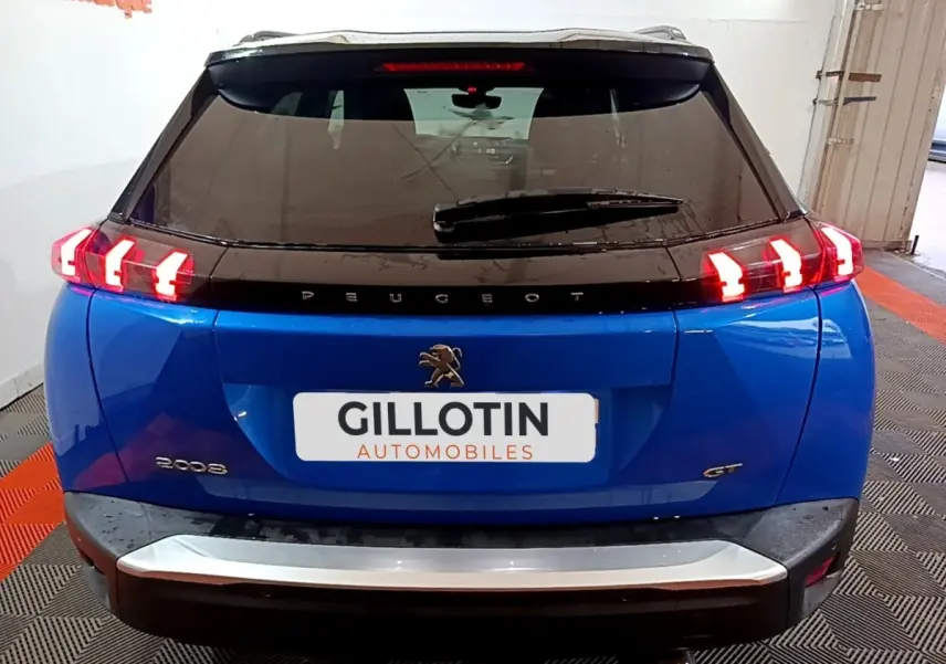 Vue arrière d’un Peugeot 2008 bleu 2021 avec feux arrière allumés et logo GT visible sur le hayon.