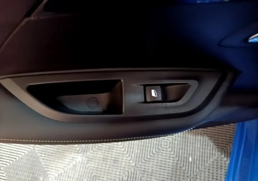 Gros plan sur la commande de lève-vitre côté gauche d’une Peugeot 2008 Bleu GT, avec couture blanche visible.