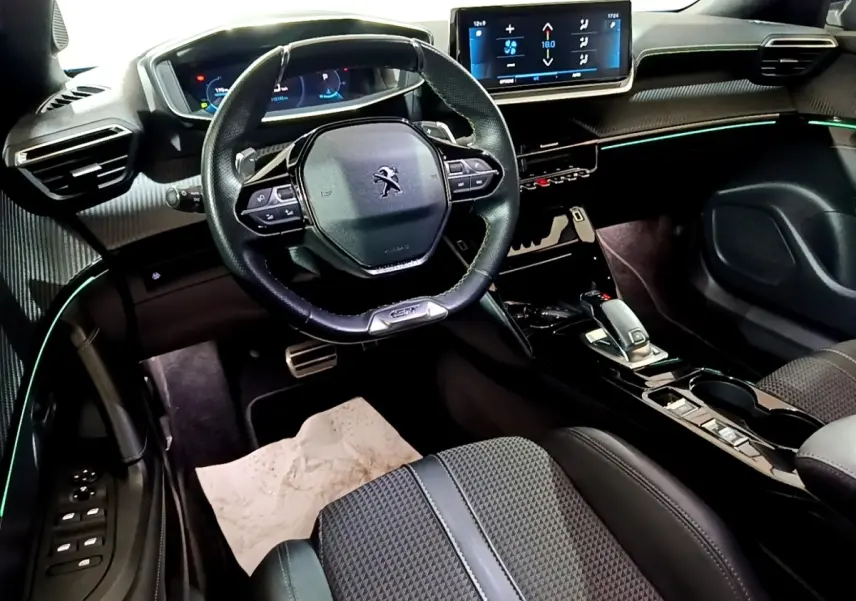 Vue intérieure côté conducteur du Peugeot 2008 Bleu, avec volant cuir compact, écran tactile 10 pouces et éclairage d'ambiance vert.