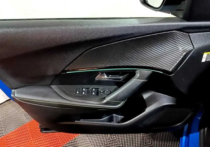 Vue intérieure côté gauche de la porte avant d’un Peugeot 2008 bleu avec insert effet carbone et éclairage d’ambiance vert.