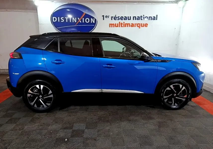 Vue de profil côté gauche d’un Peugeot 2008 GT bleu avec toit noir, roues alliage et logo GT sur l’aile avant.