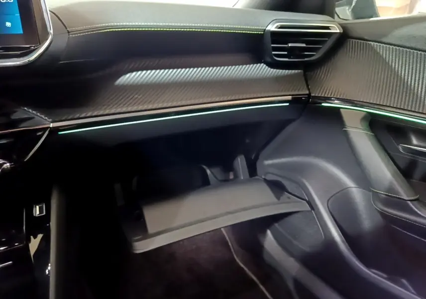 Intérieur de la Peugeot 2008 GT 2021, vue côté passager sur la boîte à gants ouverte et éclairage d’ambiance vert pâle.