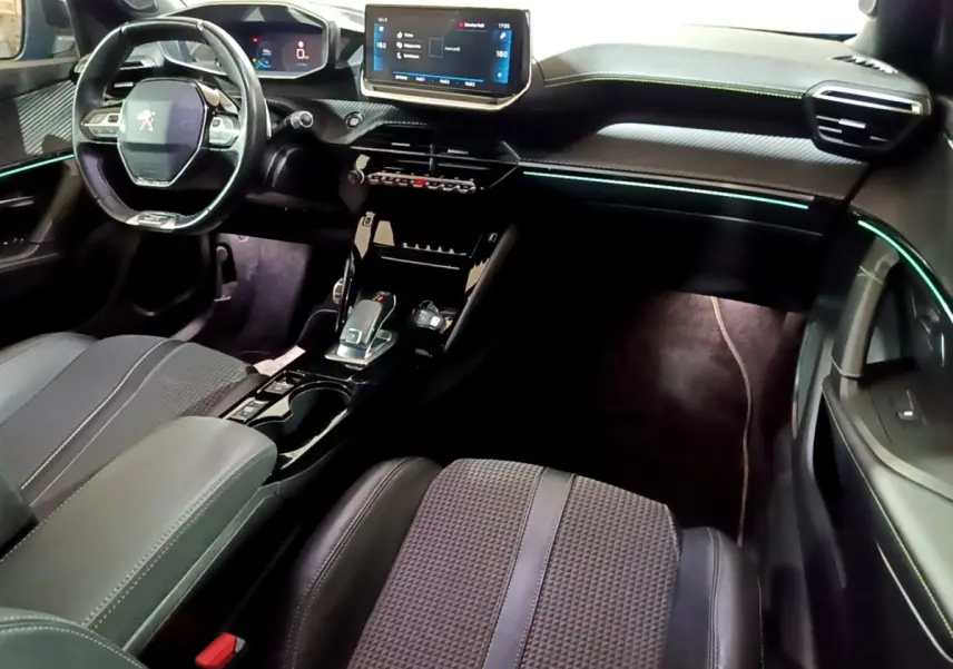 Vue intérieure avant droite du Peugeot 2008 GT 2021, tableau de bord noir avec éclairage d’ambiance bleu et écran tactile central.
