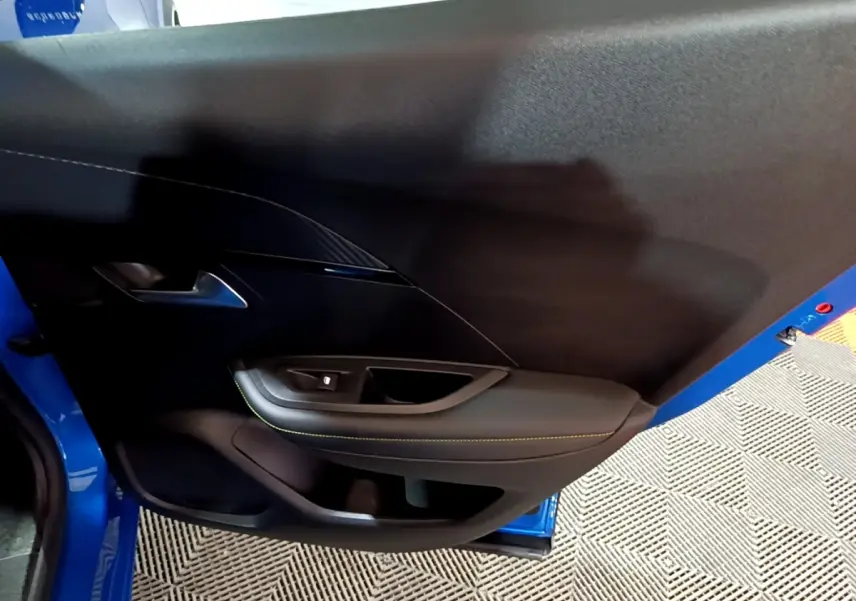 Vue intérieure du panneau de porte côté gauche du Peugeot 2008 bleu, avec surpiqûres jaunes et poignée métallique.