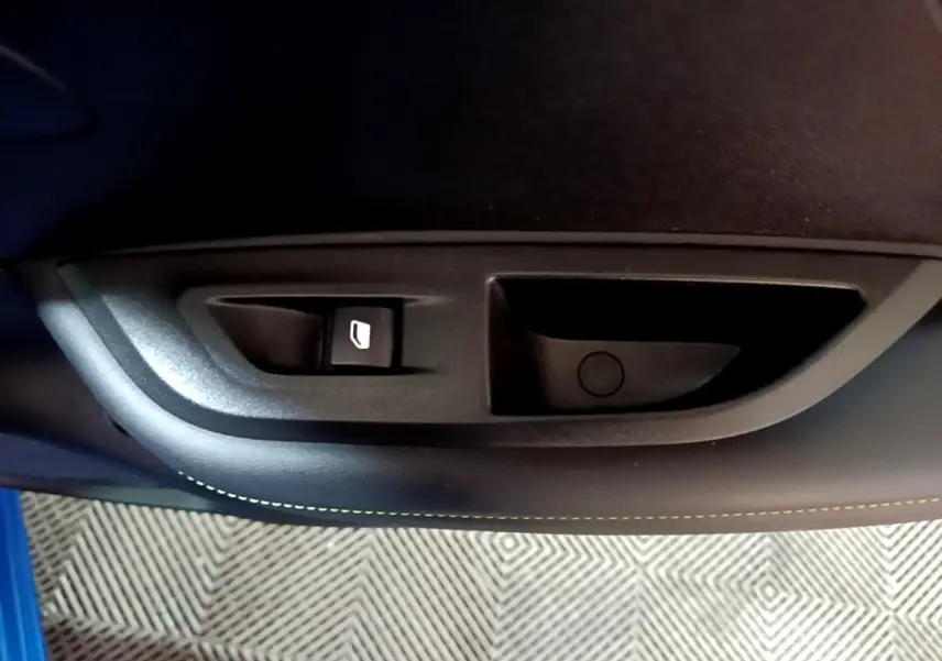 Gros plan sur la commande de lève-vitre côté gauche d’une Peugeot 2008 Bleu GT 2021, intérieur noir.