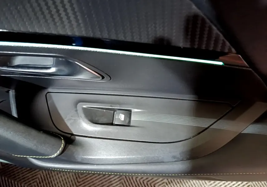 Gros plan sur la commande de lève-vitre côté gauche du Peugeot 2008 Bleu, avec insert décoratif et éclairage d’ambiance.