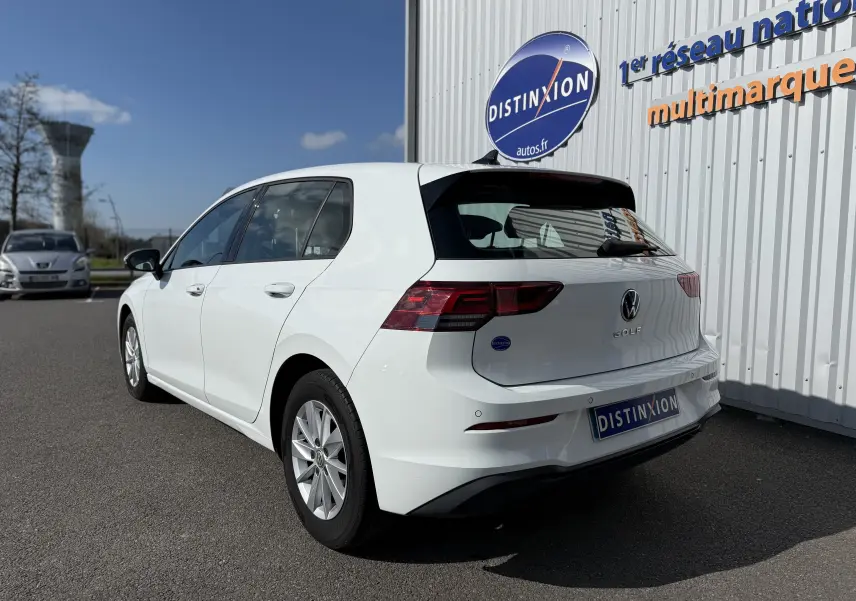 Vue 3/4 arrière droite d'une Volkswagen Golf blanche 2020 stationnée devant un bâtiment avec enseigne Distinxion.