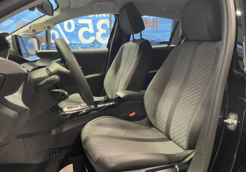 Vue intérieure côté conducteur de la Peugeot 208 noire métallisée, sièges tissu gris avec surpiqûres Quartz et volant cuir.