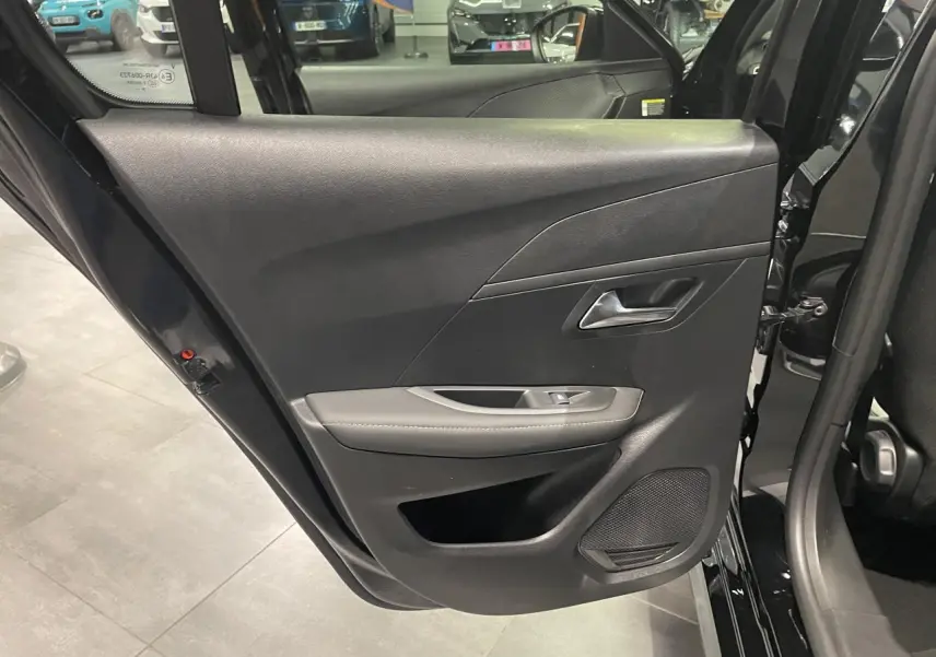 Vue intérieure de la porte arrière droite noire métallisée de la Peugeot 208 avec accoudoir gris et haut-parleur intégré.