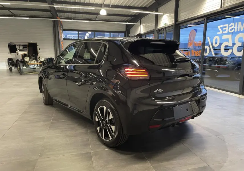 Vue 3/4 arrière droite d'une Peugeot 208 noire métallisée avec feux arrière allumés en showroom.