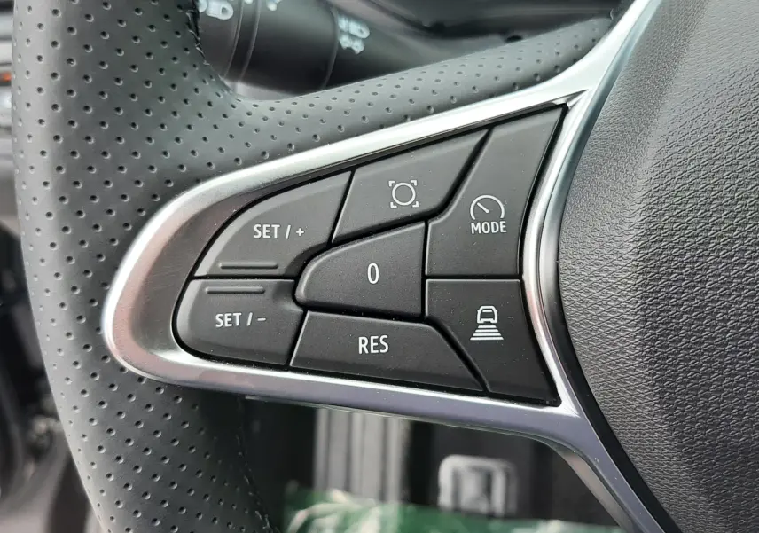 Gros plan sur les commandes à gauche du volant perforé du Renault Captur E-Tech gris cassiopée, boutons de régulateur et mode.