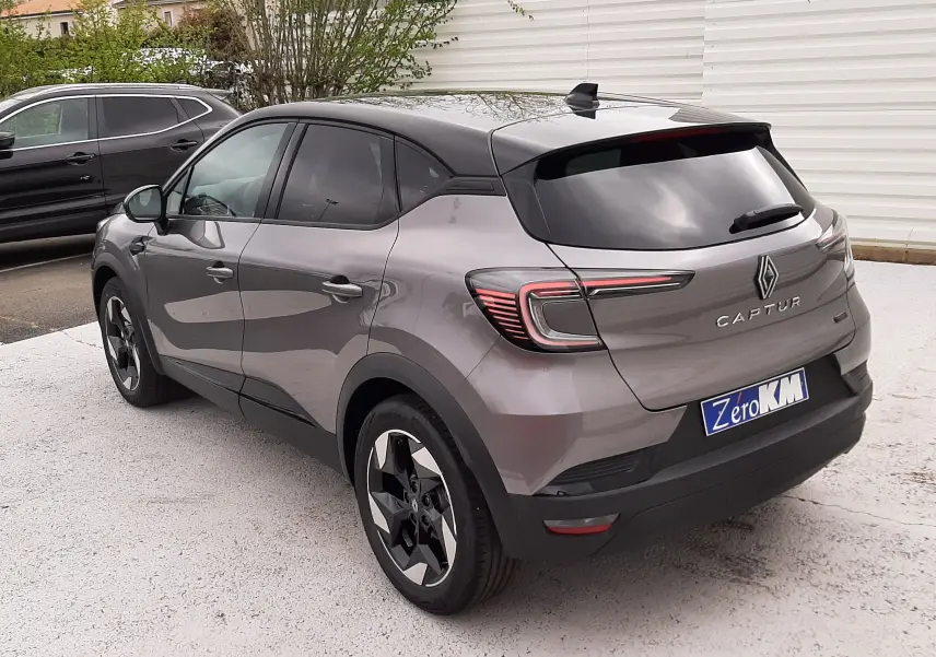 Vue 3/4 arrière droite d'un Renault Captur E-Tech Full Hybrid gris Cassiopée avec toit noir et jantes bi-ton, stationné en extérieur.