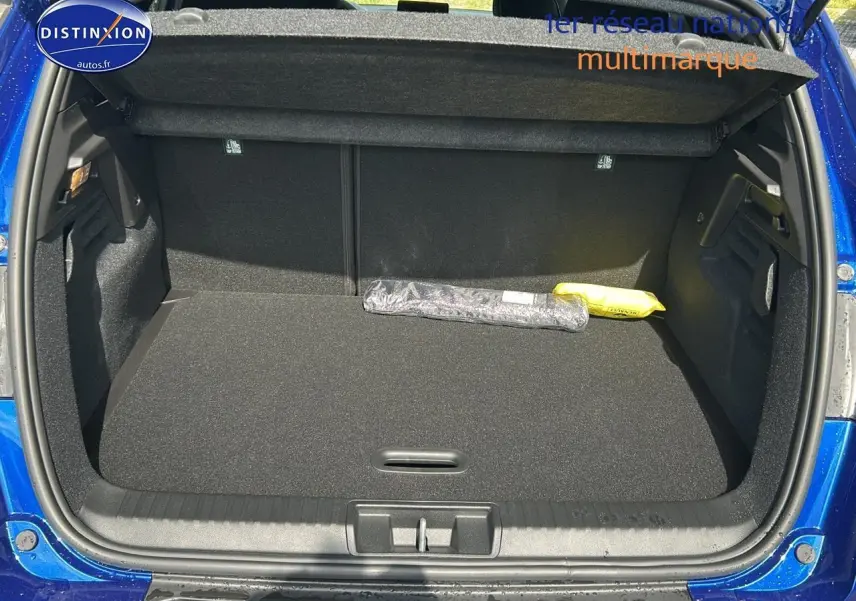 Coffre ouvert vu de l'arrière d'un Renault Captur 1.6 e-tech hybride 2025 bleu iron, avec tapis noir et objets posés.
