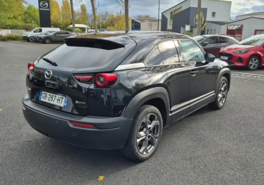 Vue 3/4 arrière droite d'un Mazda MX-30 électrique noir 2021, avec jantes spécifiques et détails de sellerie Modern Confidence.