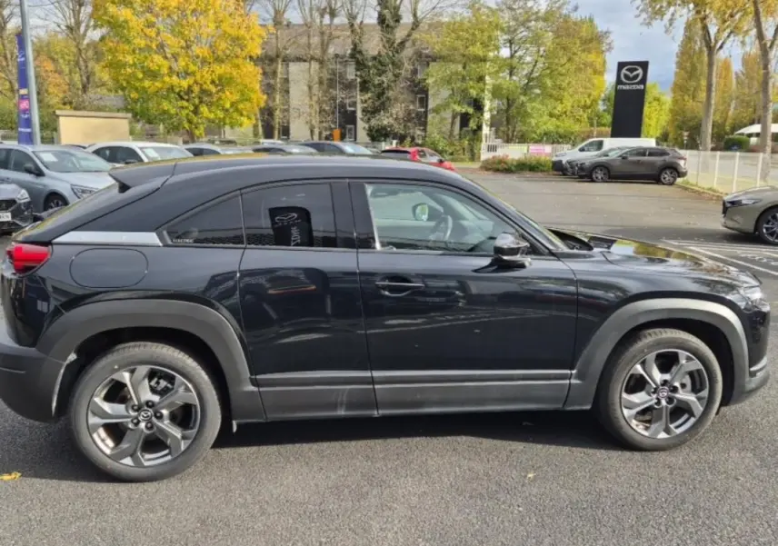 Vue de profil côté gauche d'un Mazda MX-30 électrique noir, avec jantes alliage et détails modernes en concession.