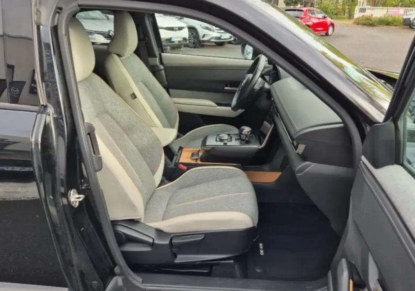 Vue intérieure côté conducteur du Mazda MX-30 2021, sellerie Modern Confidence gris clair avec inserts bois et tableau de bord noir.