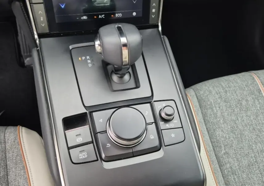 Gros plan sur la console centrale du Mazda MX-30 2021 électrique, avec levier de vitesse et molette de contrôle, sellerie grise.