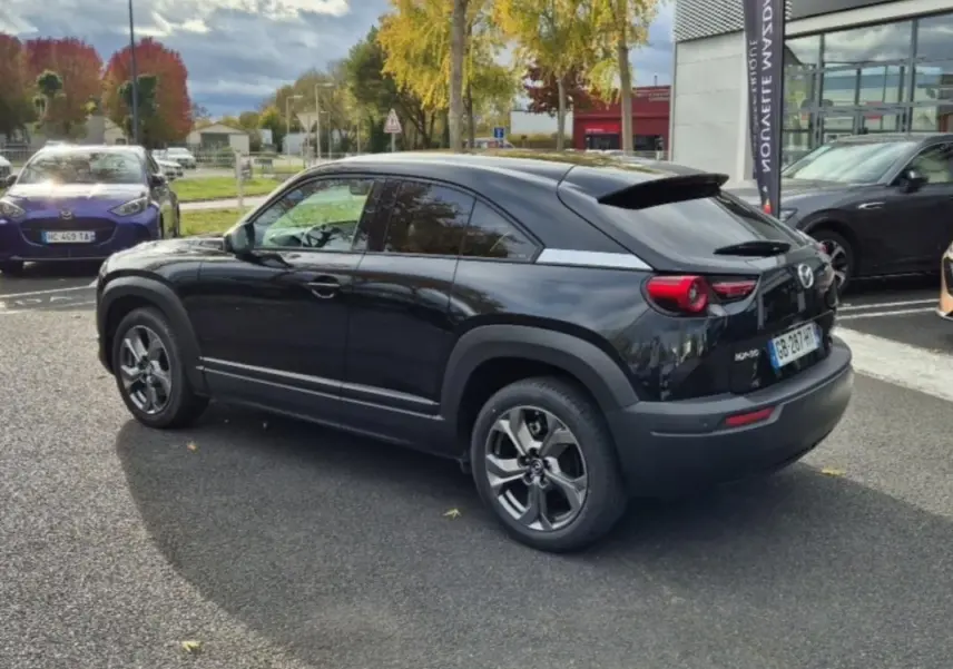 Vue 3/4 arrière droite d'un Mazda MX-30 électrique noir brillant, avec ses feux ronds distinctifs et jantes modernes.